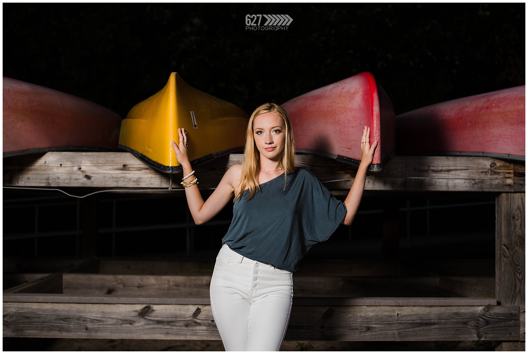 senior girl by the lake with canoes at night