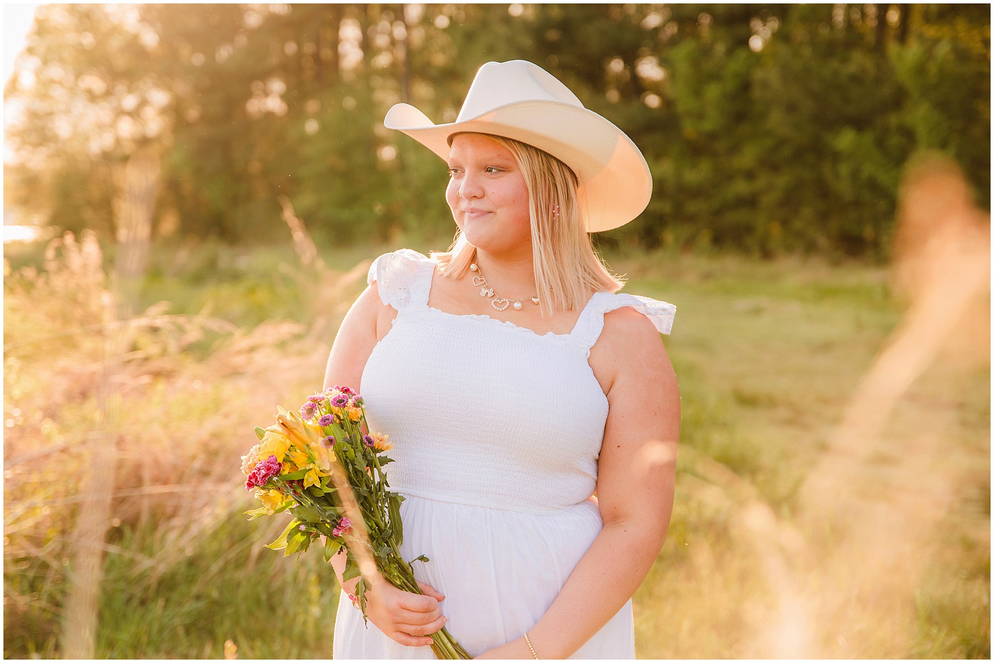 High school senior wearing a cowboy hat in the golden sunset during a country senior session.